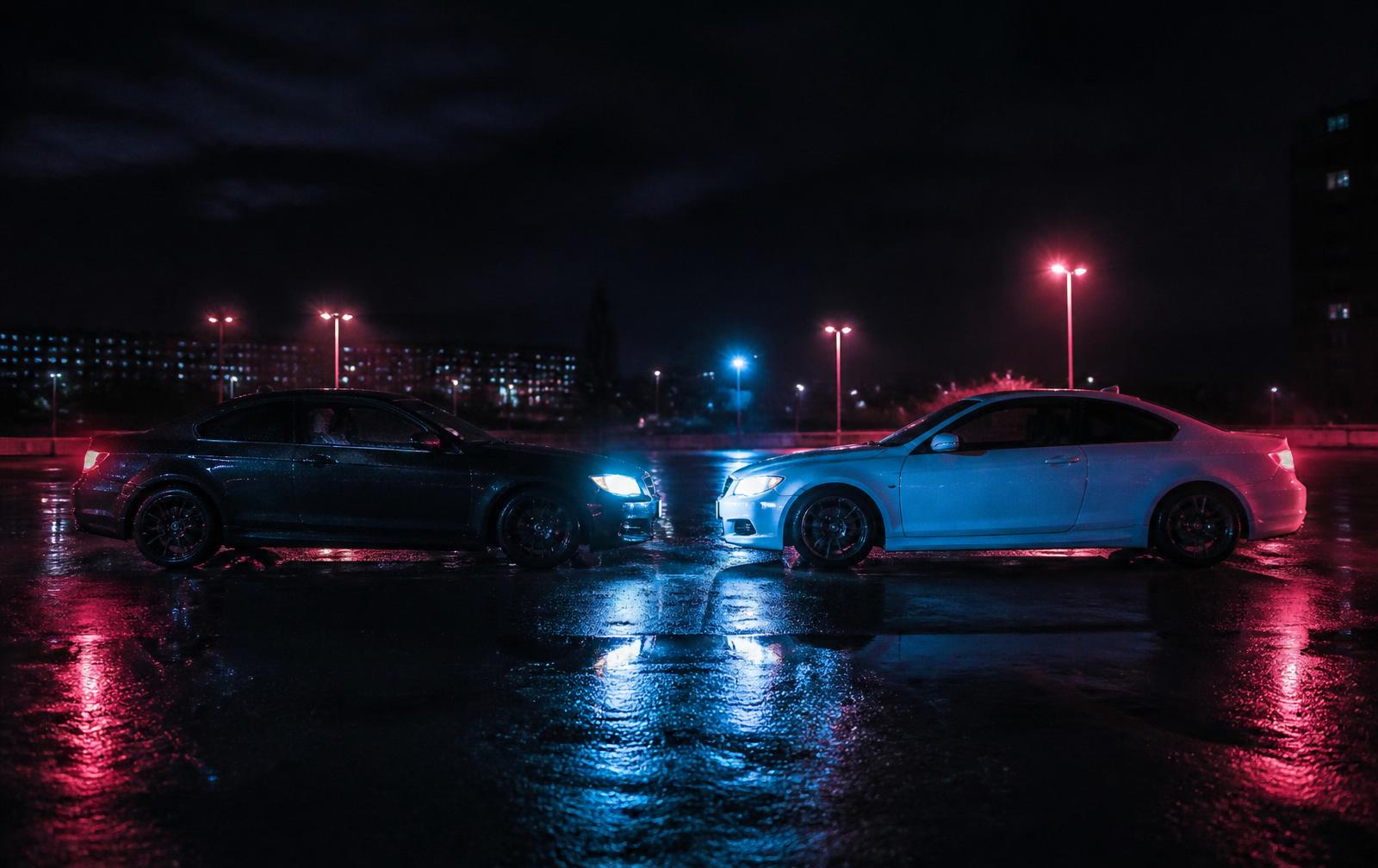 Two cars facing each other at night in a rain-slicked UK car park